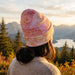 Everest Custom Full Colour Beanie - A full-colour beanie in shades of pink and orange, worn by a person against a scenic mountain backdrop.