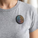 Multi-Functional Magnetic Badge - A person wearing a grey t-shirt with a round, multicoloured badge featuring a logo, attached to the chest area.