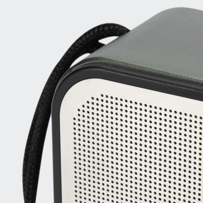 Swiss Peak 10W Bass Speaker - A grey and white portable speaker with a textured surface and a black strap attached.