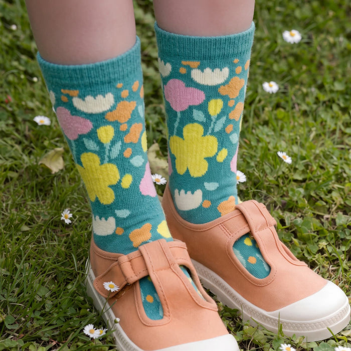 Jolly Knitted Bamboo Kids Socks - Jolly knitted bamboo kids' socks in teal with colourful floral patterns, worn with light-coloured shoes on grass.