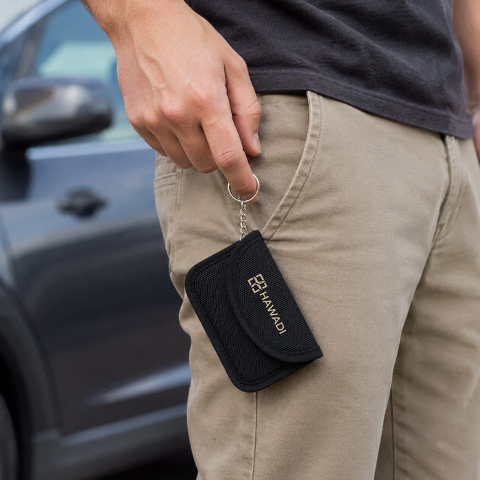 Faraday RFID Blocking Key Pouch - A black RFID blocking key pouch held by a person while standing next to a car. It has a keyring attachment.