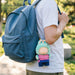 Plush Doll Jersey Outfit (15–17cm Doll) - A plush doll in a green and pink outfit attached to a blue backpack, featuring a keychain.