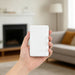 5000mAh Magnetic Wireless  Power Bank - A hand holding a white 5000mAh magnetic wireless power bank in a home setting with a fireplace and sofa in the background.
