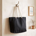 Florida GRS Recycled Beach Tote Bag - A black recycled beach tote bag with rope handles hangs on a hook against a textured wall.
