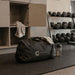 Rime Duffel Bag - A black duffel bag with a logo, resting on a table alongside a drink bottle and a towel, in a gym setting.