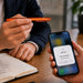 NFC Touchscreen Ballpoint Pen - An orange NFC touchscreen ballpoint pen is held above a smartphone displaying an NFC tag notification.
