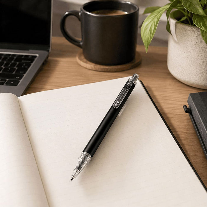 Spectrum Recycled Aluminium Ballpoint Pen - A black aluminium ballpoint pen rests on an open notebook beside a mug and a plant.