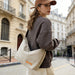 Dumpling Canvas Tote Bag - A beige canvas tote bag with a shoulder strap, worn by a person in a grey sweatshirt and tan cap, on a city street.