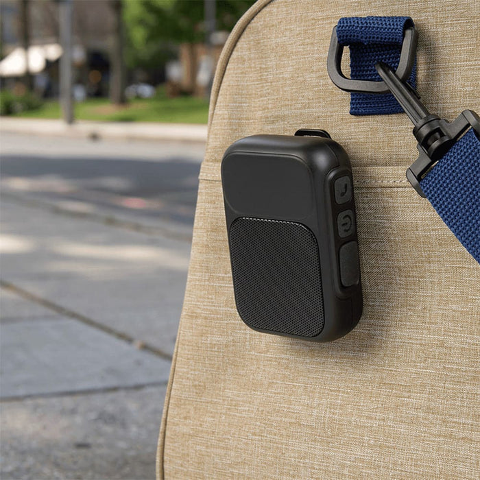 Clip Tune Magnetic Outdoor Bluetooth Speaker - A black Bluetooth speaker attached to a bag, set against an outdoor urban background. It features controls and a logo.
