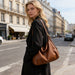 Dumpling Polyurethane Tote Bag - A brown polyurethane tote bag is worn over the shoulder by a woman in a city street setting.