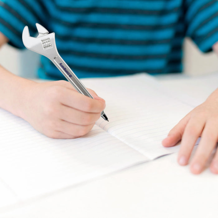 Spanner Shape Ballpoint Pen - A spanner-shaped ballpoint pen in silver, being held by a person writing on a sheet of paper.