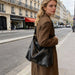 Dumpling Polyurethane Tote Bag - A black polyurethane tote bag is being carried by a model dressed in a brown coat on a Parisian street.