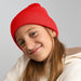 Kid Wind-S Beanie - Recycled Polyester - A red knitted beanie worn by a child with long hair, featuring a logo on the side.