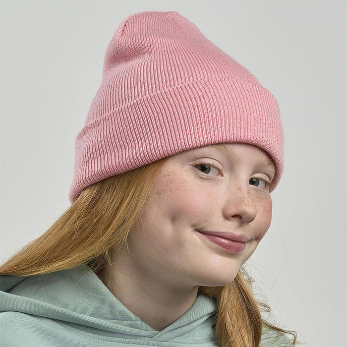 Kid Wind-S Beanie - Recycled Polyester - A pink ribbed beanie worn by a girl with red hair and freckles, featuring a logo on the side.