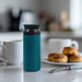 350ML/500ML Double Wall Stainless Steel Drink Bottle - A drink bottle in teal and grey sits on a table, with coffee cups and pastries in the background.