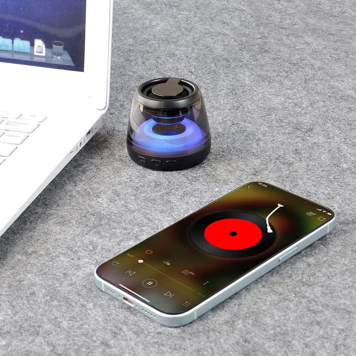 Pacific Magnetic Bluetooth Speaker Stand with RGB LED Light (Stock) - A compact black Bluetooth speaker with RGB LED light next to a smartphone displaying a music app and a laptop.