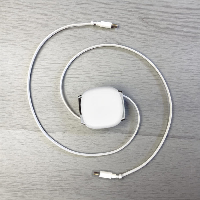 Paulo 100W Retractable Charging Data Cable - A retractable charging data cable in white, coiled with connectors at both ends, laid on a light wooden surface.
