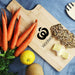Ozi Bamboo Paddle Board - A bamboo chopping board featuring a logo, with fresh carrots, a lemon, and slices of cheese on display.