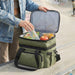 Super Duty 20 - Expanding Cooler - A green expanding cooler being filled with a water bottle, snacks, and an apple, resting on a ledge.