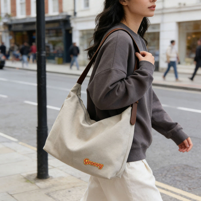 Dumpling Canvas Tote Bag - A beige canvas tote bag with brown straps, carried by a person in a grey sweater while walking on a city street.