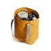 Bellroy City Tote - A mustard yellow tote bag filled with a blanket, headphones, and various accessories, featuring grey straps.