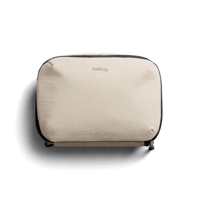 Bellroy Lite Tech Kit - A beige tech kit with a zip closure and a logo on the front, featuring a textured fabric design.