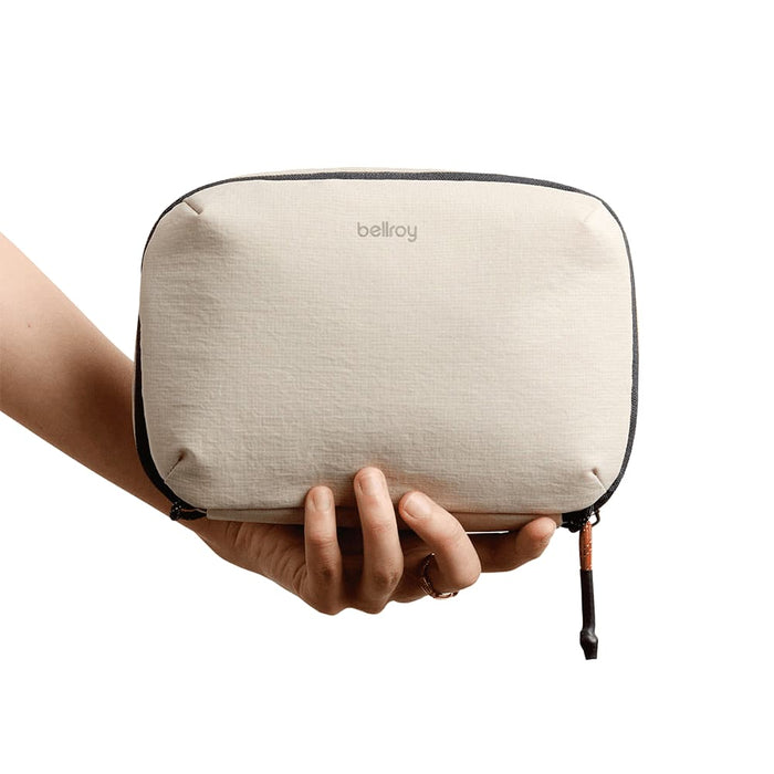 Bellroy Lite Tech Kit - A hand holds a tan Bellroy Lite Tech Kit, featuring a soft-textured exterior and a zip closure.