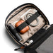 Bellroy Lite Tech Kit - A tech kit featuring a grey exterior, tan interior, drink bottle, earphones, charging cables, and a pen.