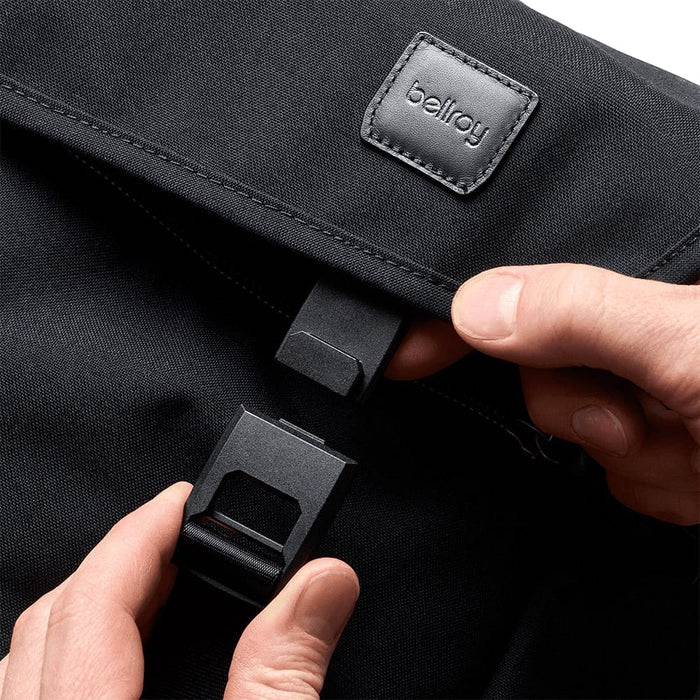 Bellroy Classic Messenger 13L - A black messenger bag with a flap and fastening mechanism, featuring a logo. A hand is holding the clasp.