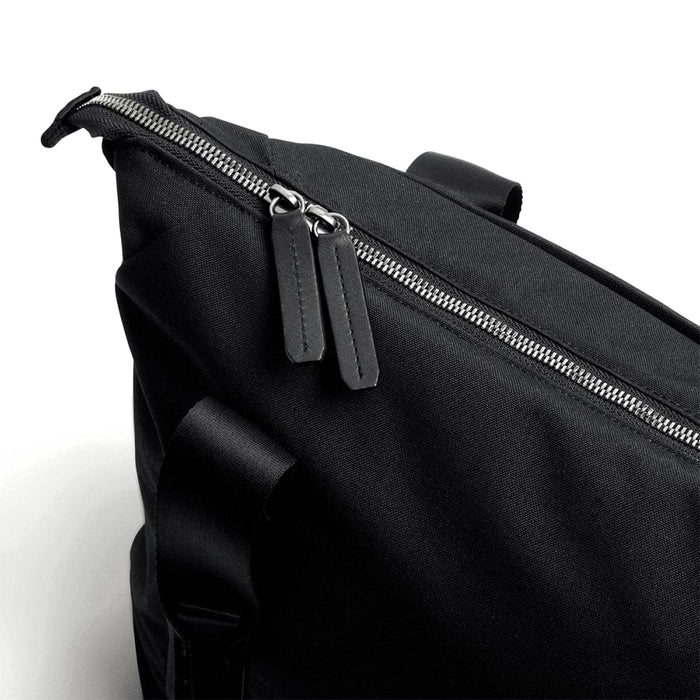 Bellroy Classic Tote - A black tote bag features a zip closure with leather zip pulls and a sturdy handle. It has a sleek, minimal design.