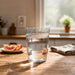 Tritan Carry Cup - A clear glass filled with water, placed on a wooden table beside a plate of sliced fruit and a towel.