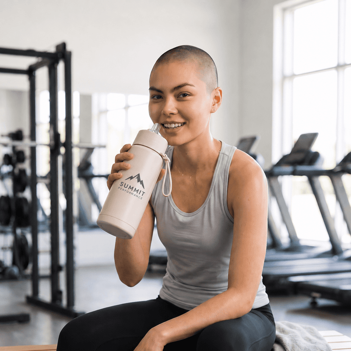 The Sofia 1L Bottle - A drink bottle in light grey with a logo, held by a smiling person in a gym setting.