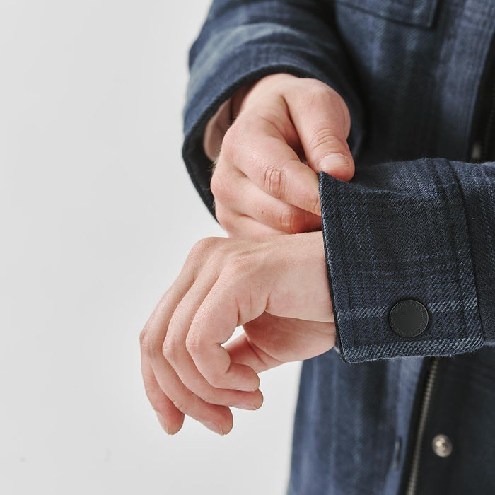 Women's Highland Sherpa Lined Plaid Jacket - A plaid jacket in a dark blue hue, featuring a Sherpa lining and buttoned cuffs, is being showcased with hands adjusting the sleeve.