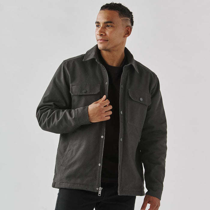 Men's Oxide Sherpa Lined Canvas Jacket - A men's dark grey Sherpa lined canvas jacket with front pockets and a collared neckline. It has a subtle logo.