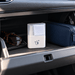 Zoe Spray & Wipe Cleanser - A white spray and wipe cleanser with a cleaning cloth, placed inside a car's glove compartment alongside sunglasses and a dark blue pouch.