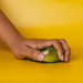 Jelly Cube Sensory Toy - A green jelly cube sensory toy being squeezed by a hand, set against a bright yellow background.