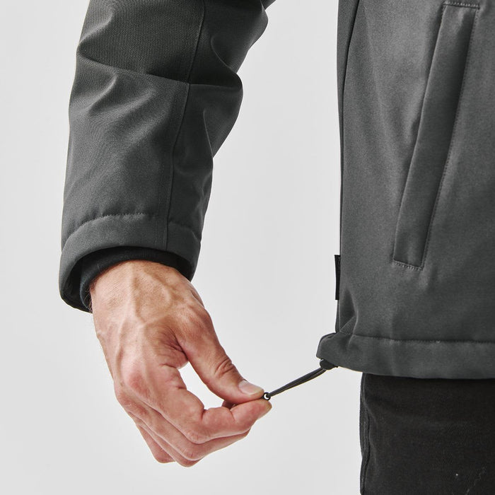 Men's Athabasca Thermal Jacket - A hand adjusting the hem of a men's thermal jacket in a dark colour, featuring a logo on its side.
