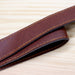 Saint-Rémy Cooler Basket - A brown leather strap with yellow stitching, laid on a wooden surface. The strap has a smooth finish and a sturdy appearance.