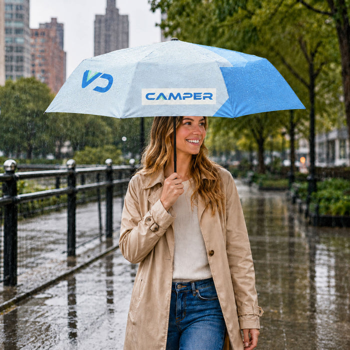 21'' Anti-rebound Folding Umbrella - A light blue and white folding umbrella held by a woman wearing a beige trench coat, standing in the rain.