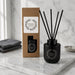 Botanical Reed Diffuser – 150ml - A black botanical reed diffuser with essential jasmine fragrance, accompanied by a brown box and black sticks, on a marble surface.