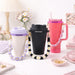 Woven Flower Tumbler Strap - A drink bottle with a woven flower strap in black, pink, and purple, displayed on a pastel-themed table.