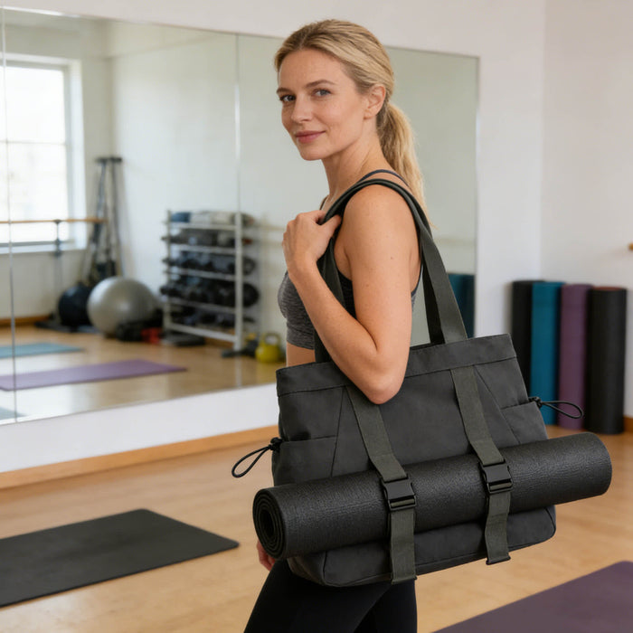Lightweight Tote Bag With Yoga Mat Straps - A black tote bag with yoga mat straps is being carried by a person in a fitness studio. The bag has a logo.