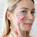 Ice Massager Roller Double Head - A pink double-headed ice massager roller held near a woman's face, featuring a logo on the handle.