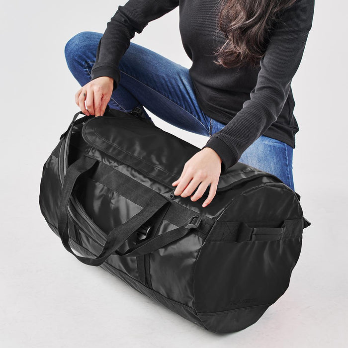 Stormtech Gear Bag Medium - A black duffle bag is being held by a person in casual attire, positioned on a white background.