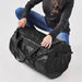 Stormtech Gear Bag Medium - A black duffle bag is being held by a person in casual attire, positioned on a white background.