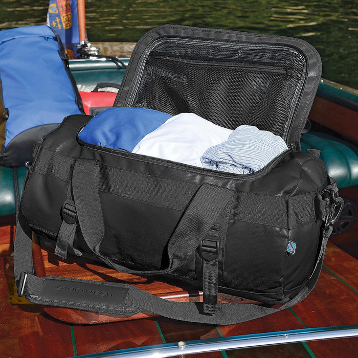 Stormtech Gear Bag Small - A black duffle bag with clothes inside, featuring a zippered top and a logo on the side.