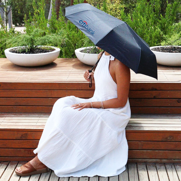Poppins Umbrella - A black umbrella rests over a person wearing a white dress, seated on wooden decking surrounded by planters.