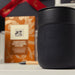 Branded Tech Kit Gift Pack - A black branded mug with a logo in the foreground, set against a patterned gift box and a pen.
