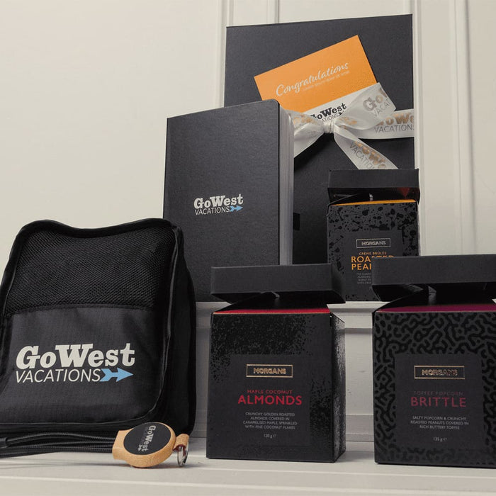 The Custom Travel Kit - A black bag with a logo, three gift boxes containing snacks, and an orange card with a ribbon.