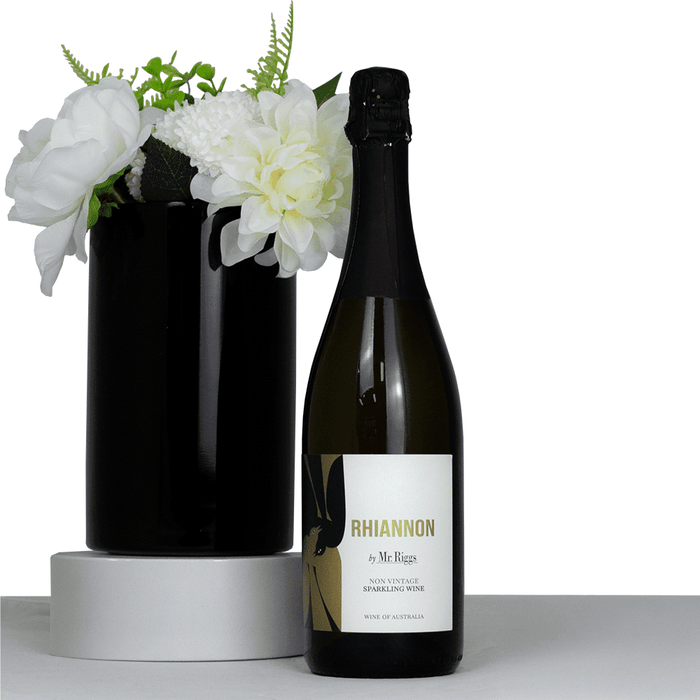 The Entertainer Set - A sparkling wine bottle with a black label next to a black vase filled with white flowers.